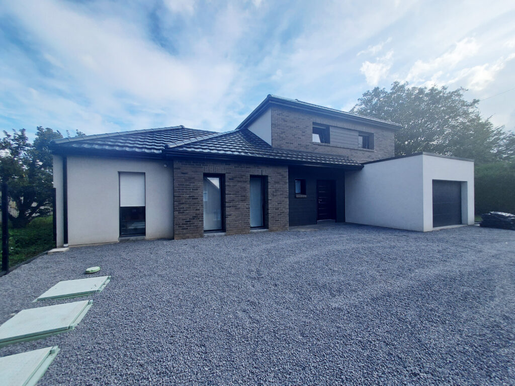 Maison moderne avec façade en enduit et briques et garage attenant. Cour avant recouverte de gravier gris.