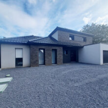 Maison moderne avec façade en enduit et briques et garage attenant. Cour avant recouverte de gravier gris.