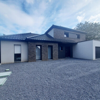 Maison moderne avec façade en enduit et briques et garage attenant. Cour avant recouverte de gravier gris.